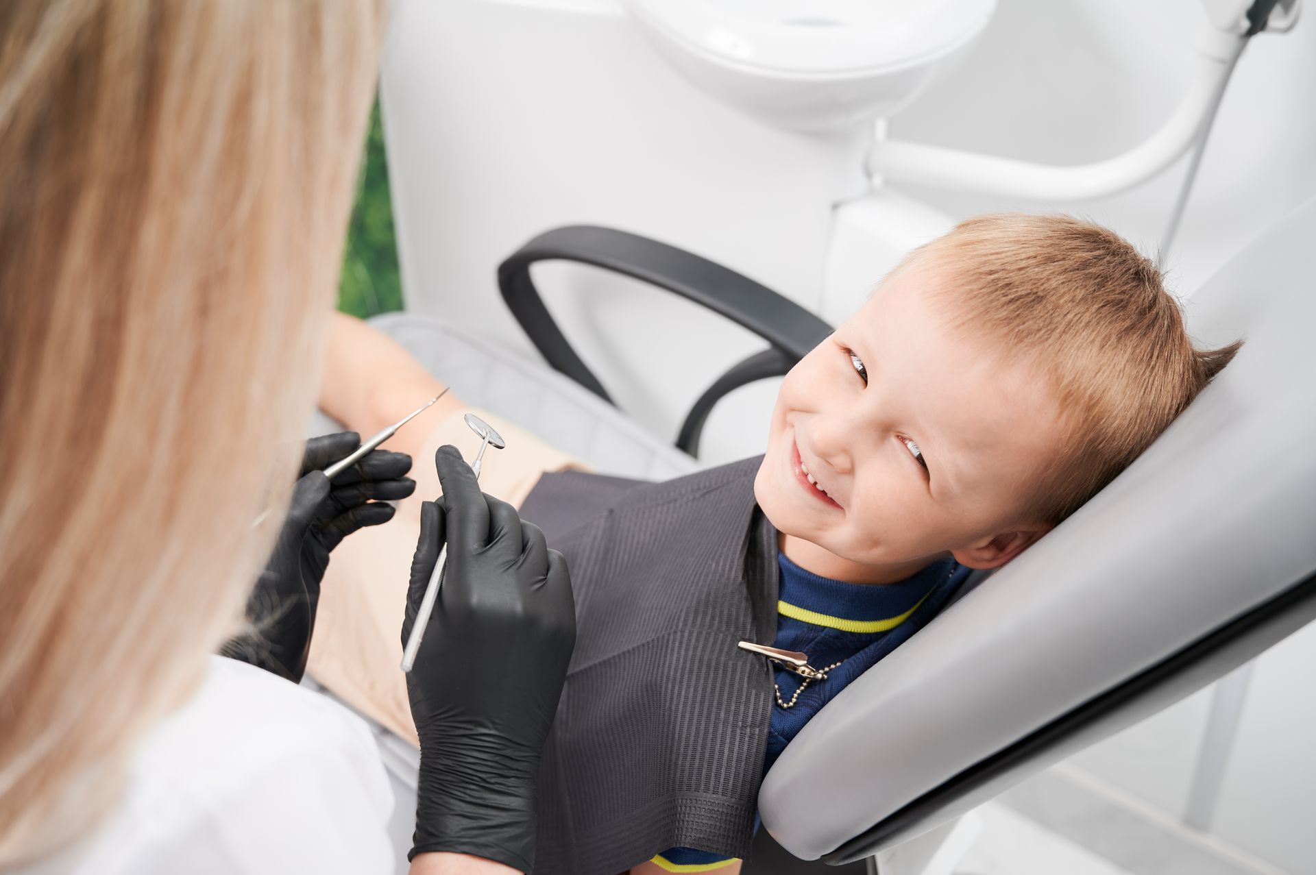 A young boy is sitting in a dental chair while a dentist examines his teeth.
