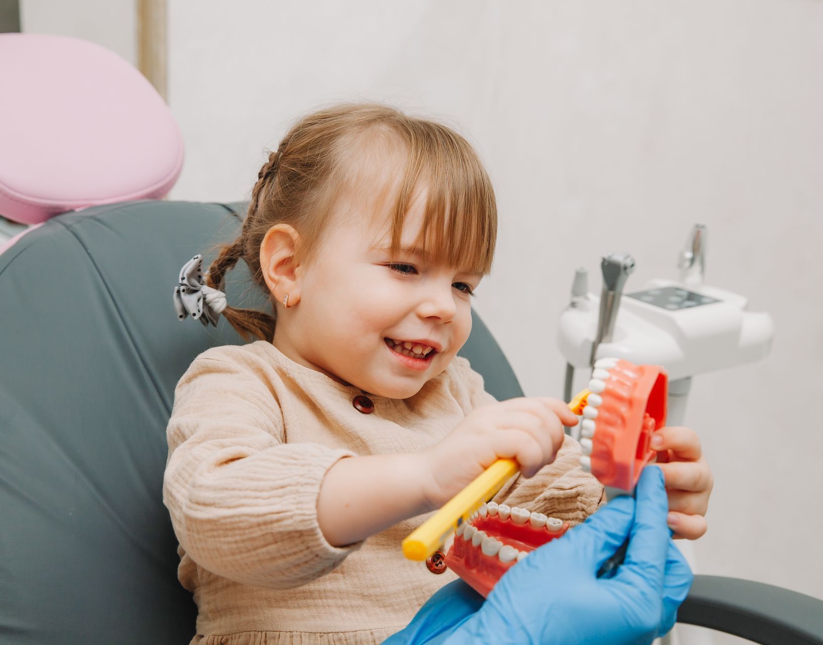 A little girl is brushing her teeth with a toothbrush in a dental office.