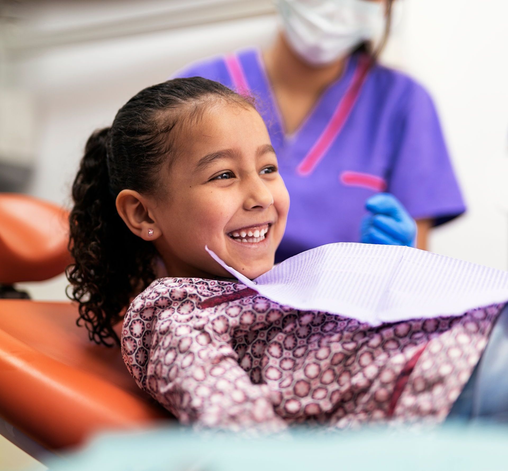 A little girl is smiling while sitting in a dental chair.