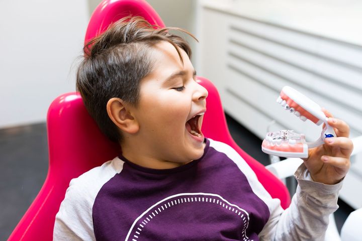 A young boy is sitting in a dental chair holding a model of teeth | Pediatric dentist near Tarrytown NY