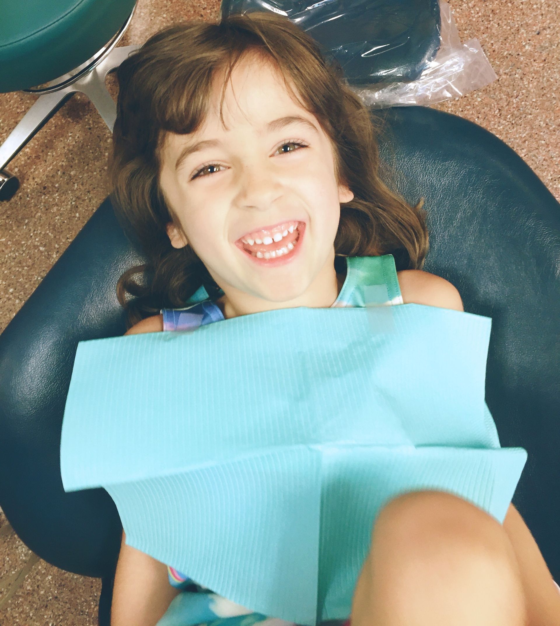 Little girl smiling, laying in a dentist chair.