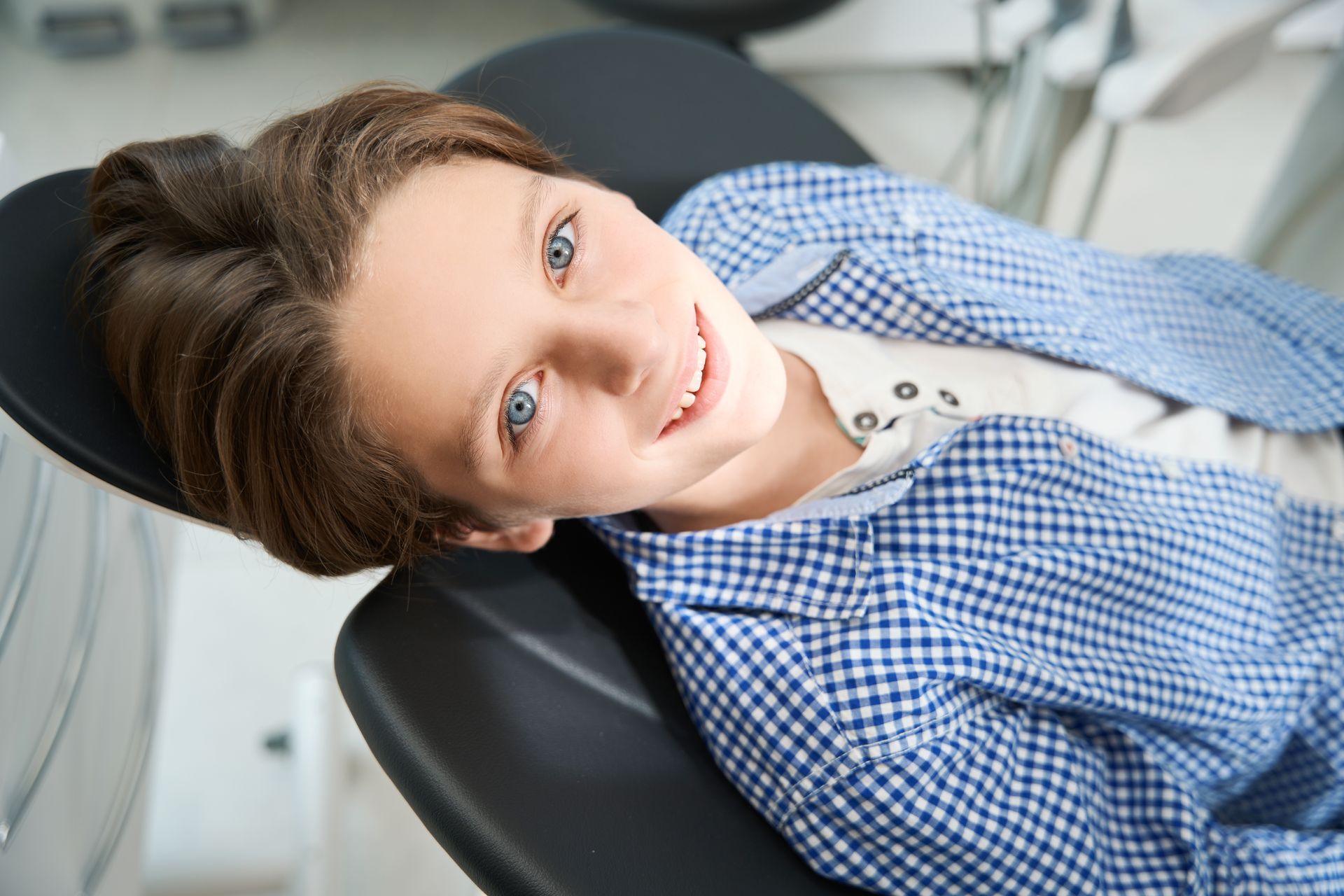 A young boy is laying in a dental chair and smiling at the camera.