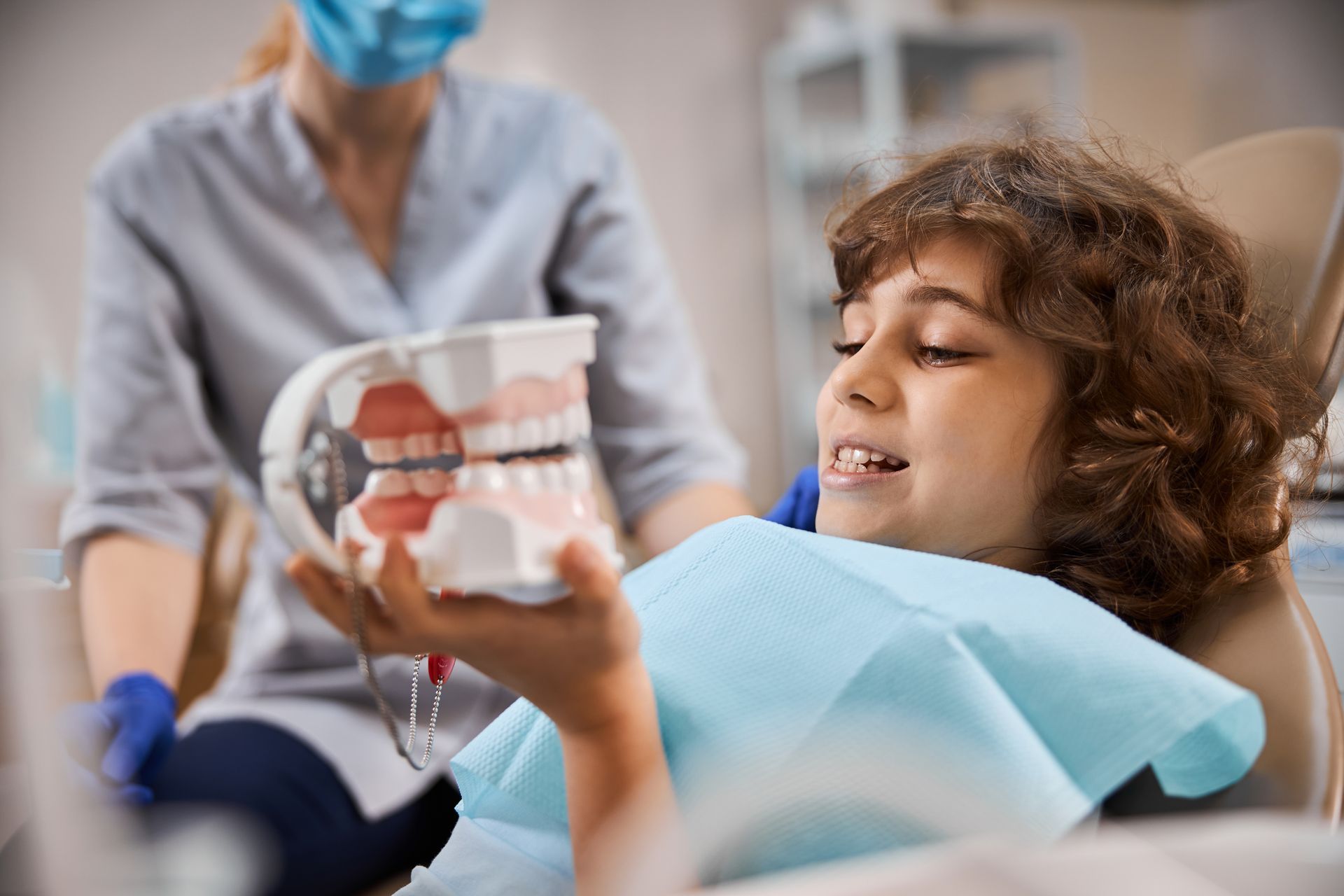 A young boy is sitting in a dental chair holding a model of his teeth. pediatric dental emergency care near Tarrytown, NY.