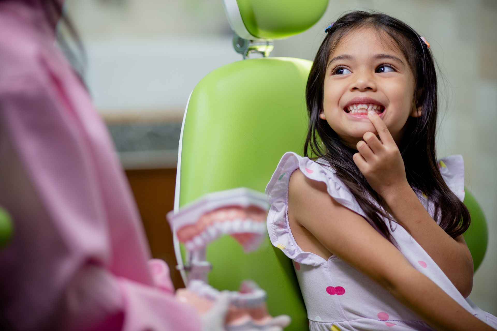 A little girl is sitting in a dental chair and smiling at the pediatric dentist.