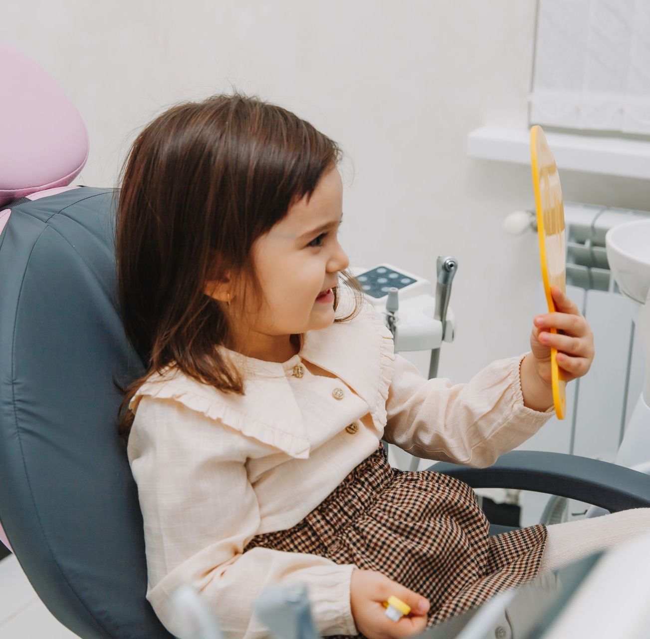 A little girl is sitting in a dental chair looking at herself in a mirror, dental fillings in Tarrytown, NY
