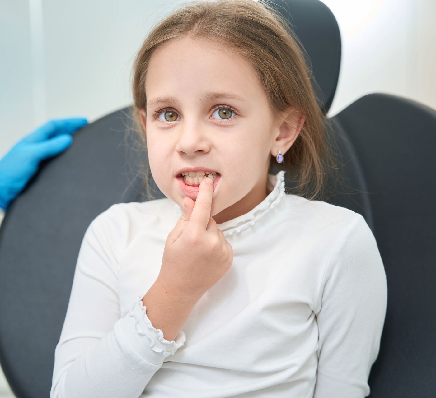 A little girl with toothache is sitting in a dental chair with her finger in her mouth. Quality emergency dental care
