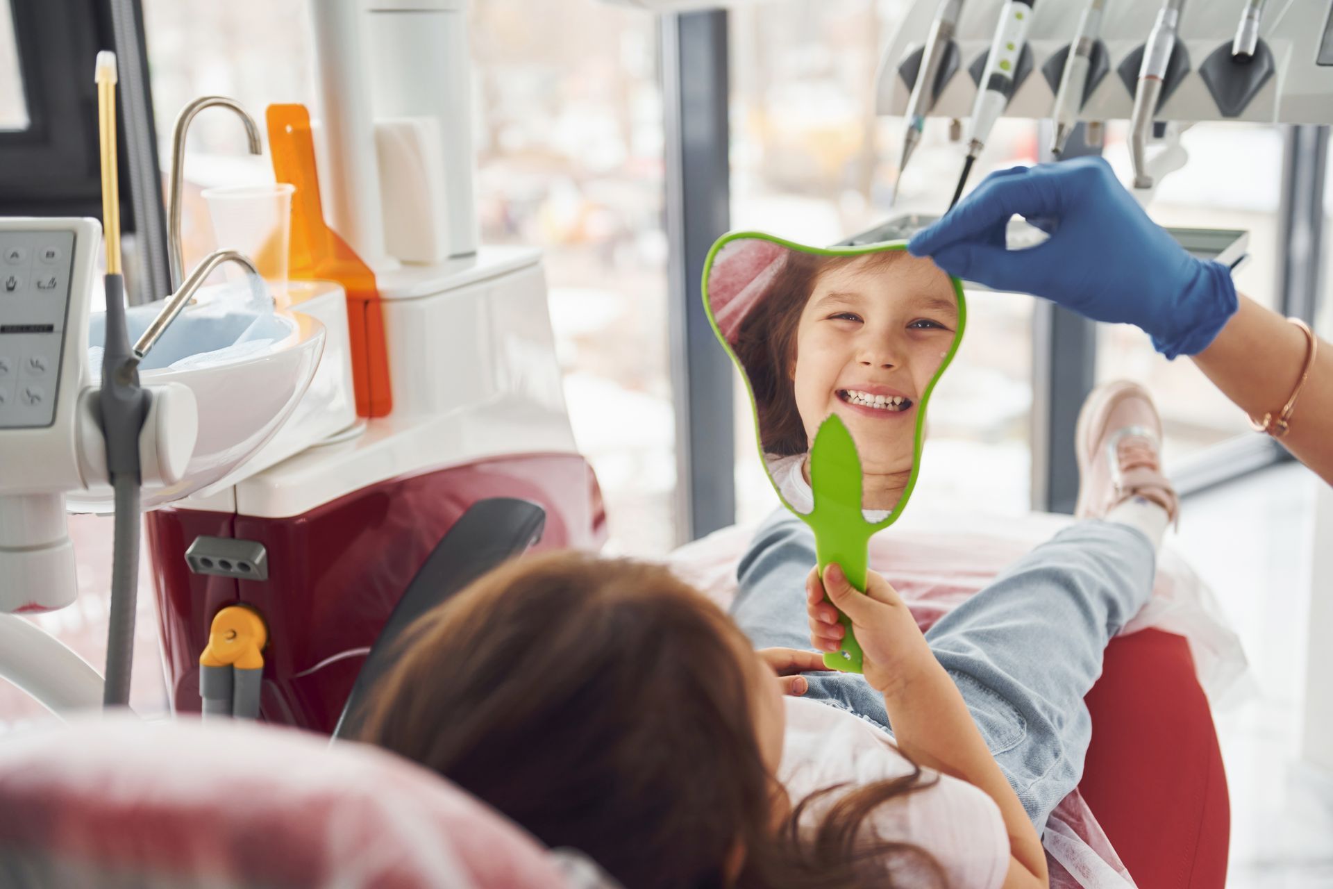 A little girl is looking at her teeth in a mirror at the dentist. Expert dentist for kids in Tarrytown, NY
