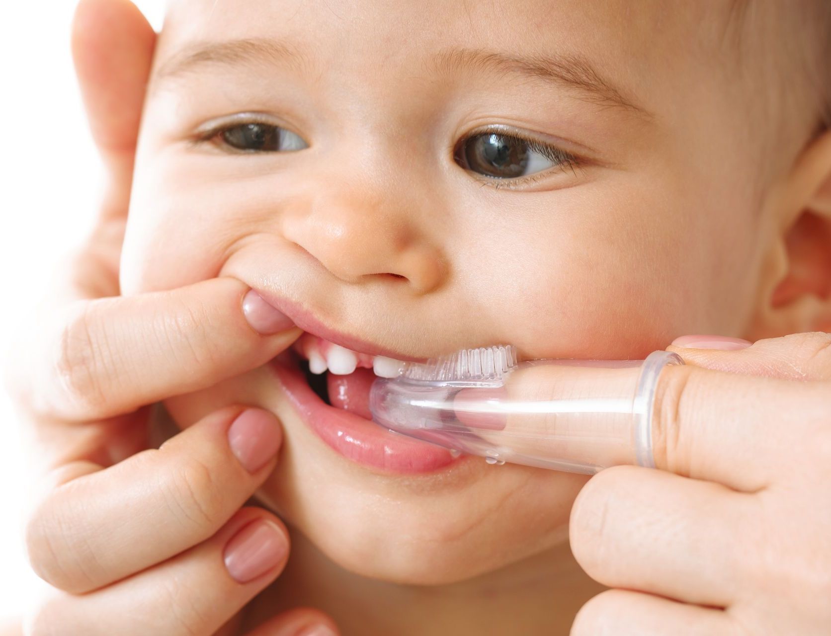 A woman is brushing a baby 's teeth with a finger toothbrush.