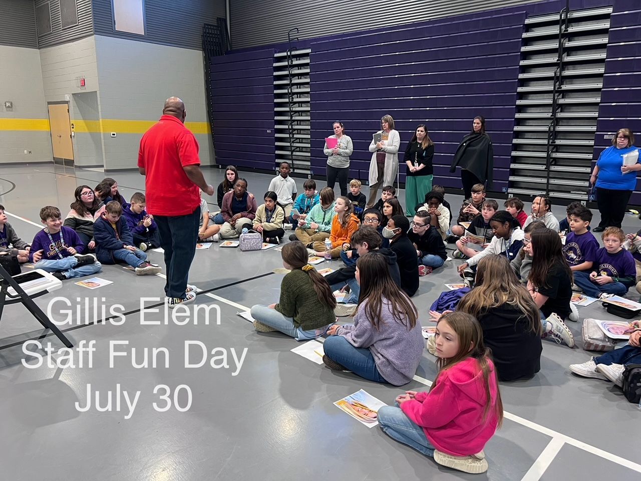 A group of children are sitting on the floor in a gym.