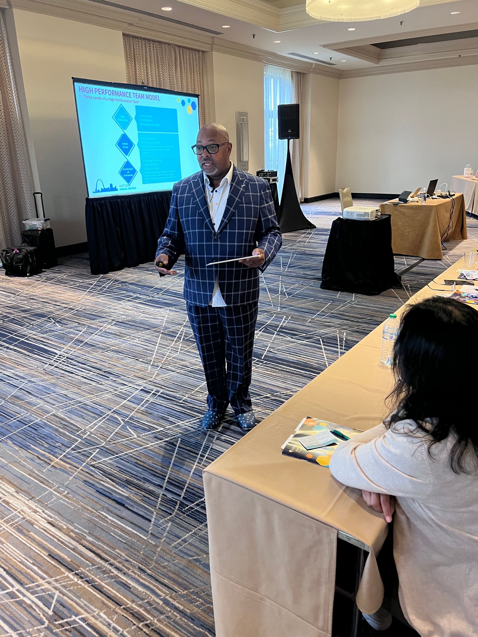 A man in a plaid suit is giving a presentation in a conference room.