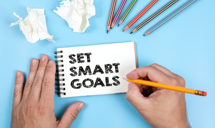 A person is writing on a piece of paper that says set smart goals.