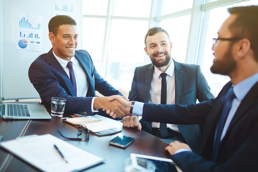 A group of businessmen are shaking hands while sitting at a table.