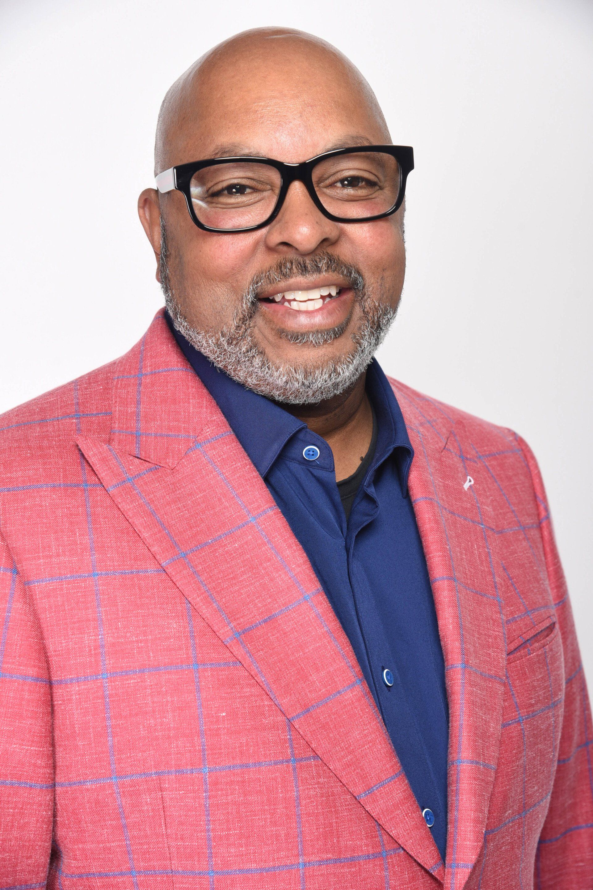A man wearing glasses and a red jacket is smiling for the camera.