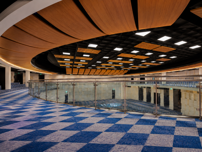Empty modern hall with blue checkered floor, curved wood ceiling, and glass railing around a central area