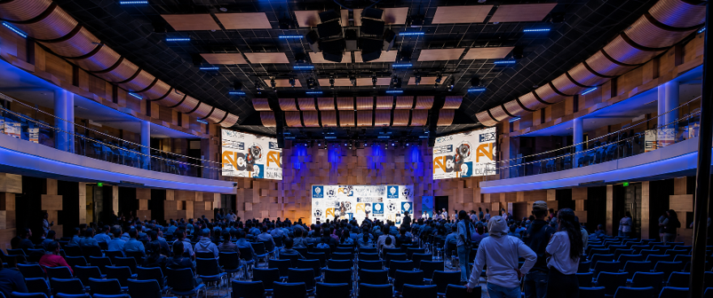 Large auditorium with blue seats and a lit stage during a conference or performance