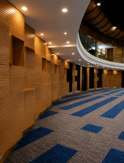Curved indoor corridor with warm wood walls, recessed lights, and blue-gray patterned carpet