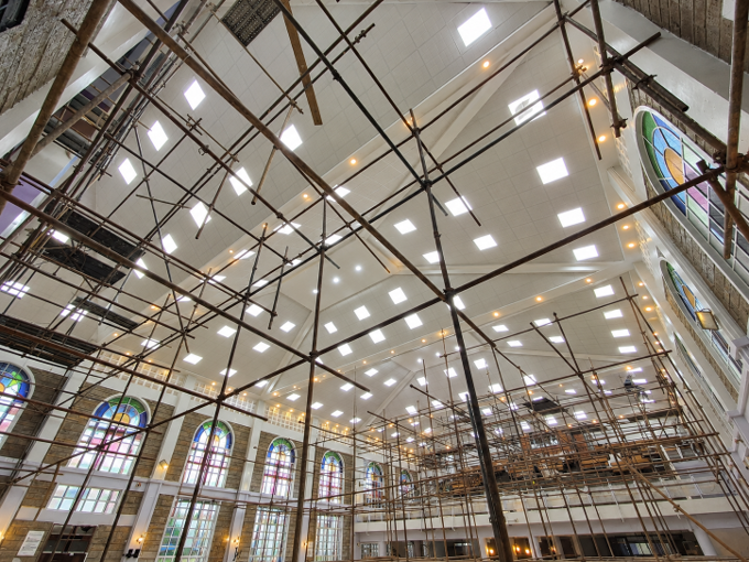 Cathedral interior under renovation with scaffolding, arched stained-glass windows, and bright ceiling lights