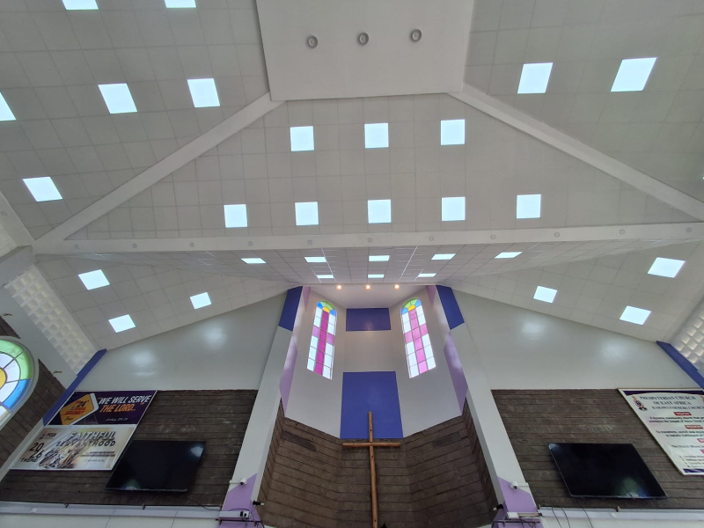 Interior of a modern church sanctuary with a high ceiling, colorful stained-glass windows, and a central cross