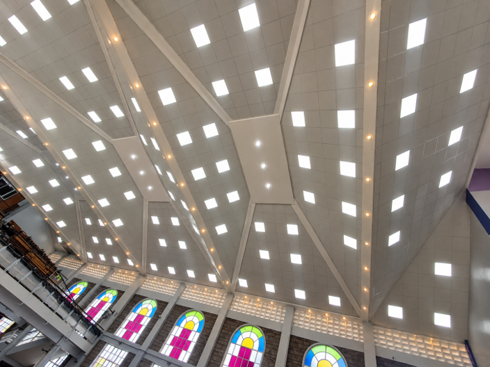 Stadium ceiling with bright square lights and colorful stained-glass windows along the upper wall