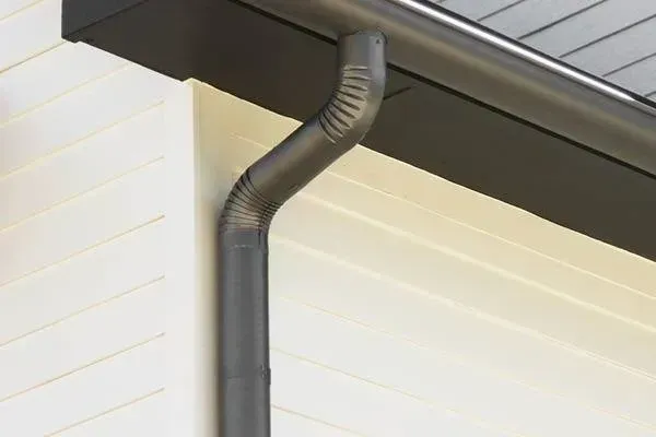 A close up of a gutter on the side of a house with a tree in the background.