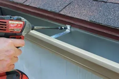 A person is using a milwaukee drill to install a gutter on a roof.