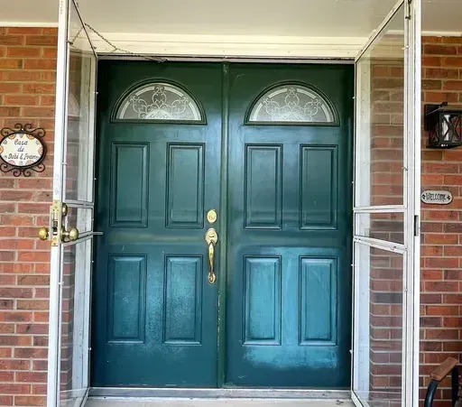 The front door of a brick house with a green double door.