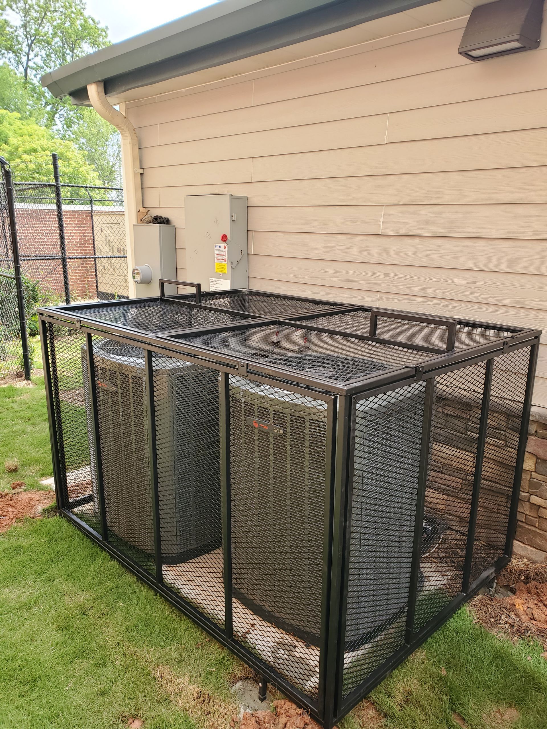 Two air conditioners are sitting inside of a metal cage on the side of a house.