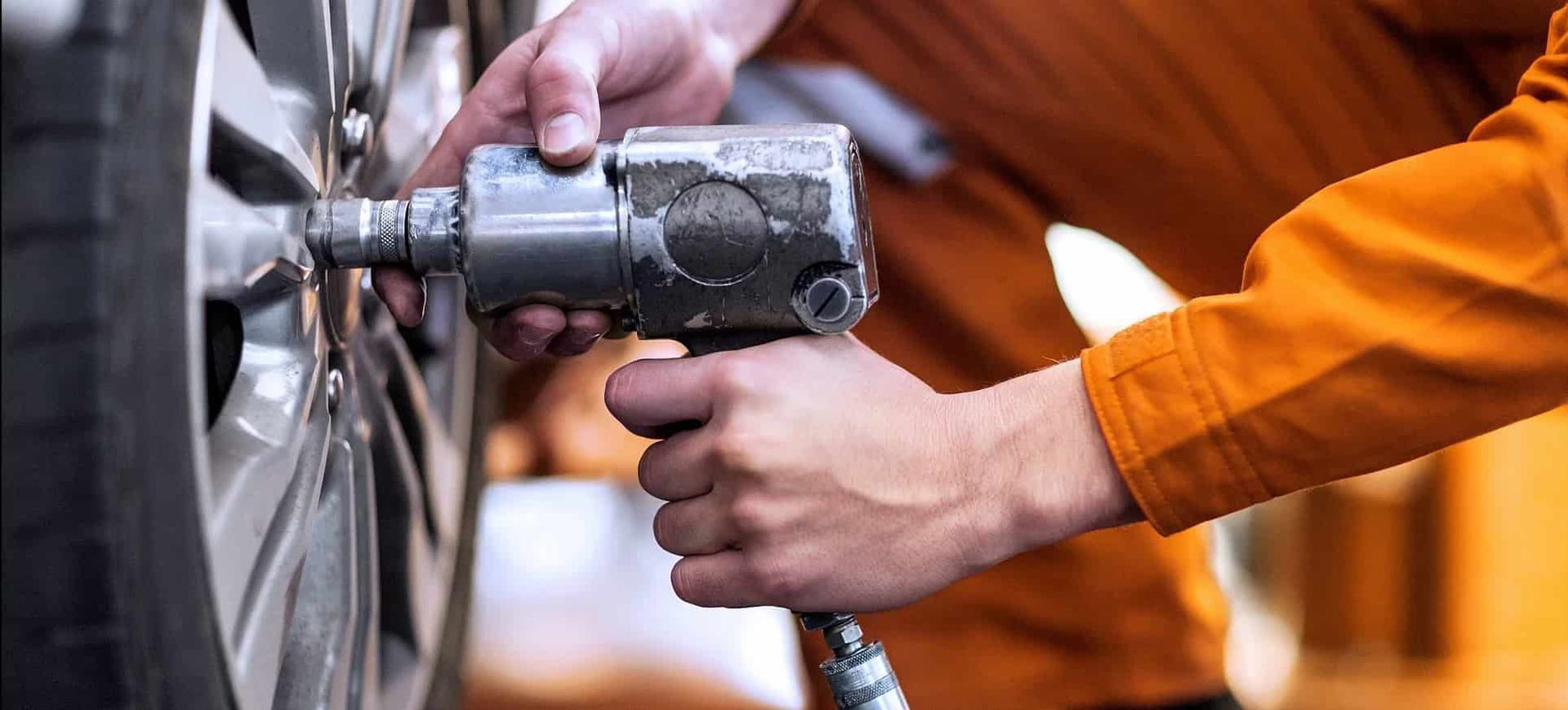 A Man Is Using An Air Wrench To Change A Tire On A Car — Sojos Mechanical & Tyre Service In Kariong, NSW