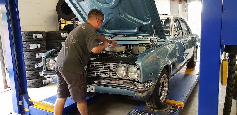 A Man Is Working On A Blue Car In A Garage — Sojos Mechanical & Tyre Service In West Gosford, NSW