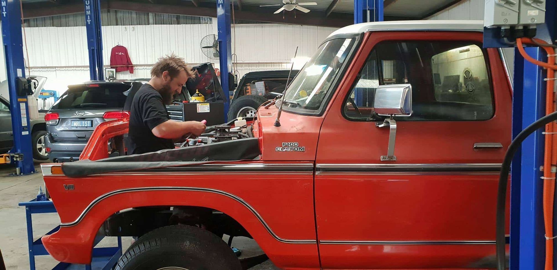 A Man Is Working On A Red Truck In A Garage — Sojos Mechanical & Tyre Service In West Gosford, NSW