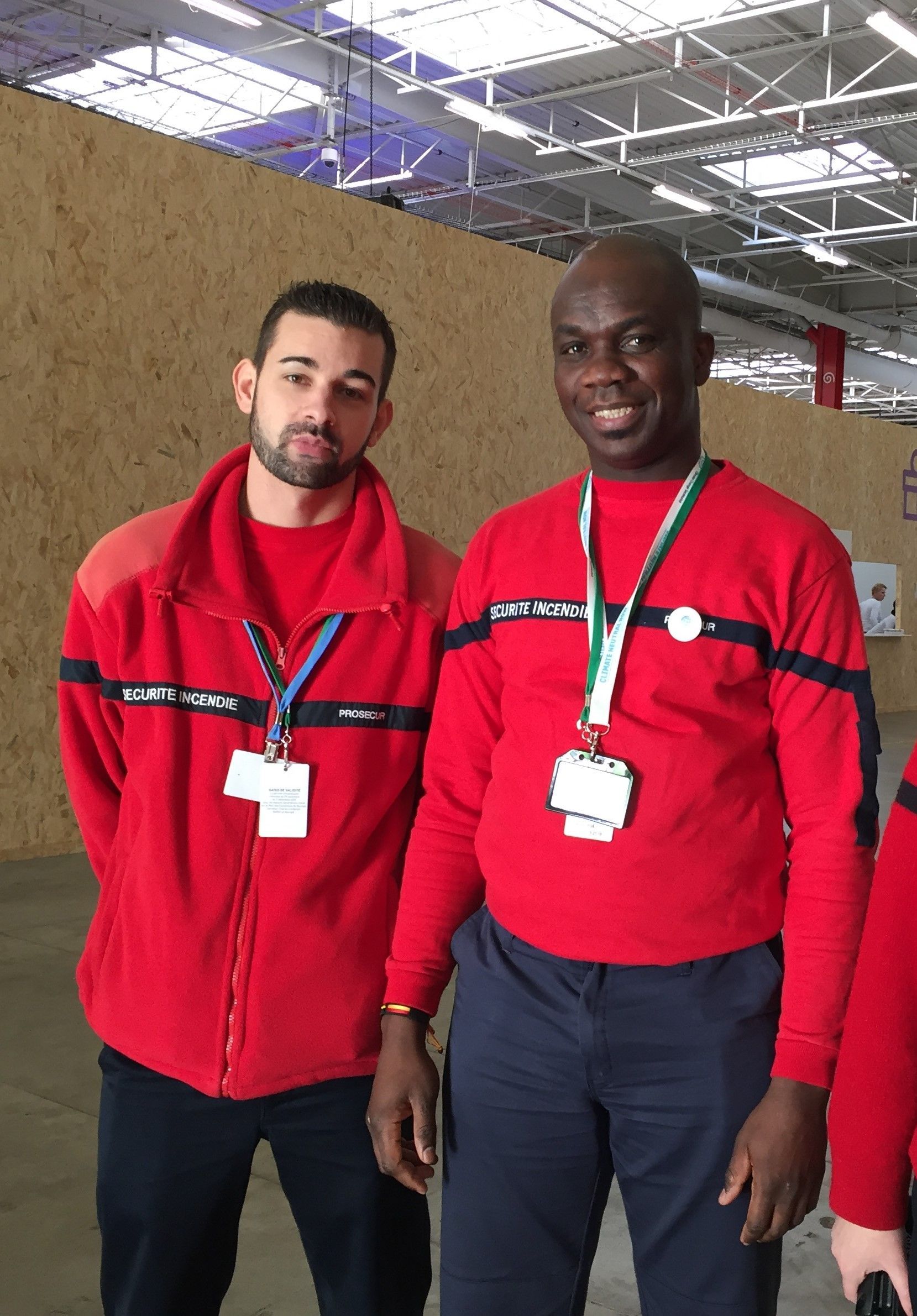 Deux hommes en chemises rouges se tiennent l'un à côté de l'autre dans un entrepôt.