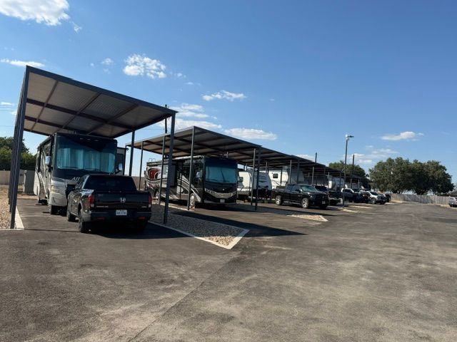Covered parking lot with several vehicles, including trucks and a black SUV, under metal canopies.