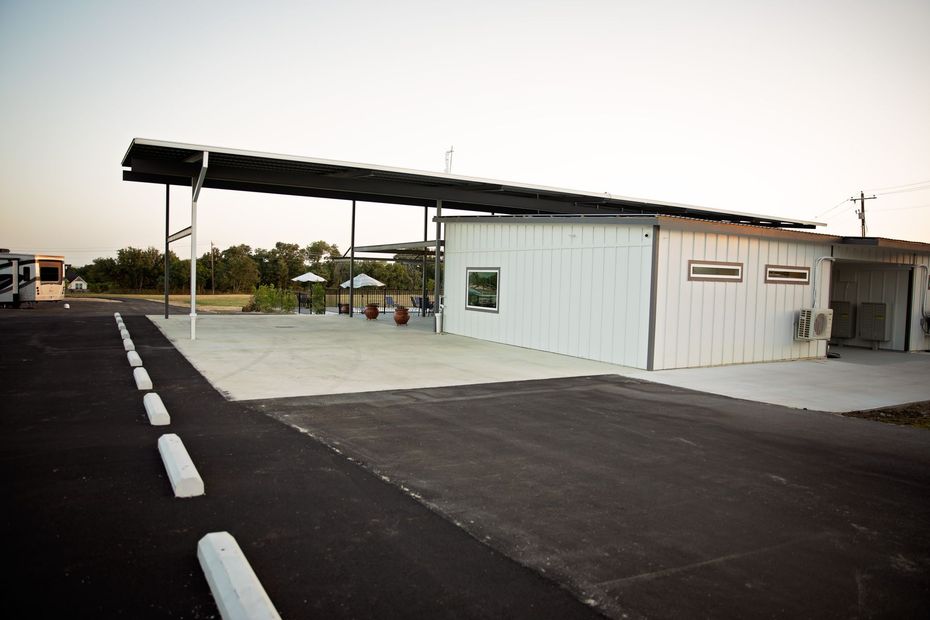 Small white building with a black canopy beside an empty paved lot at dusk