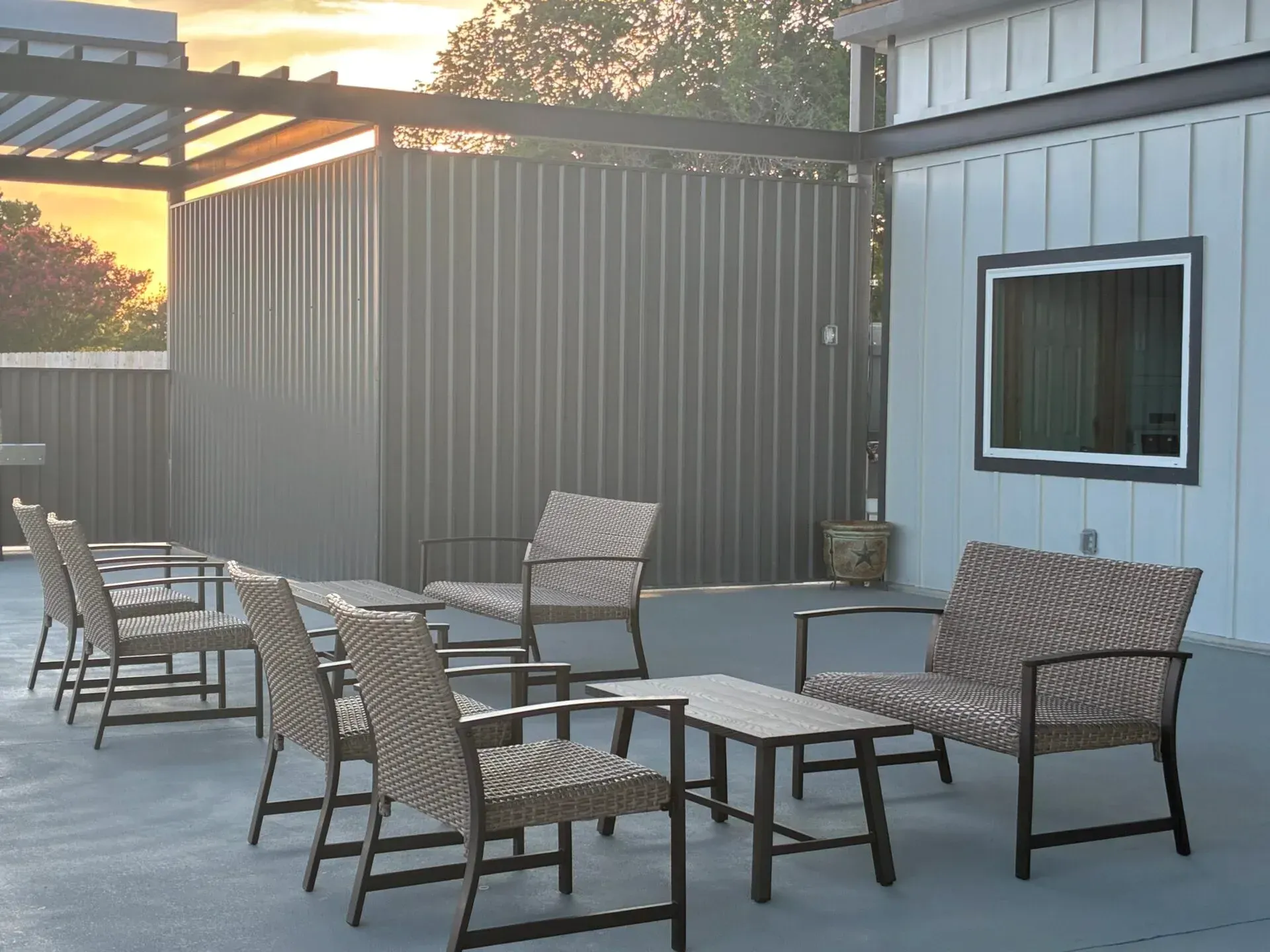 Sunlit rooftop patio with metal pergola, seating, potted plants, and railing at sunset