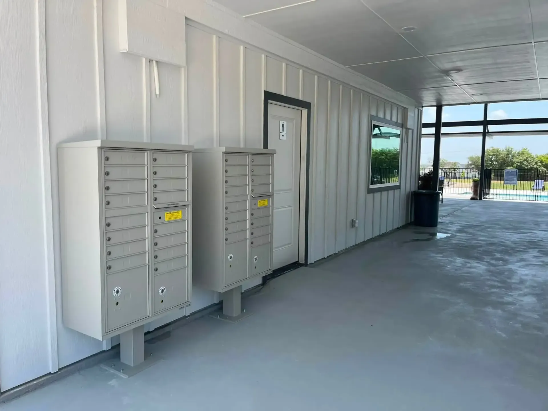 Mailboxes on a white building wall beside a door and outdoor walkway in bright daylight