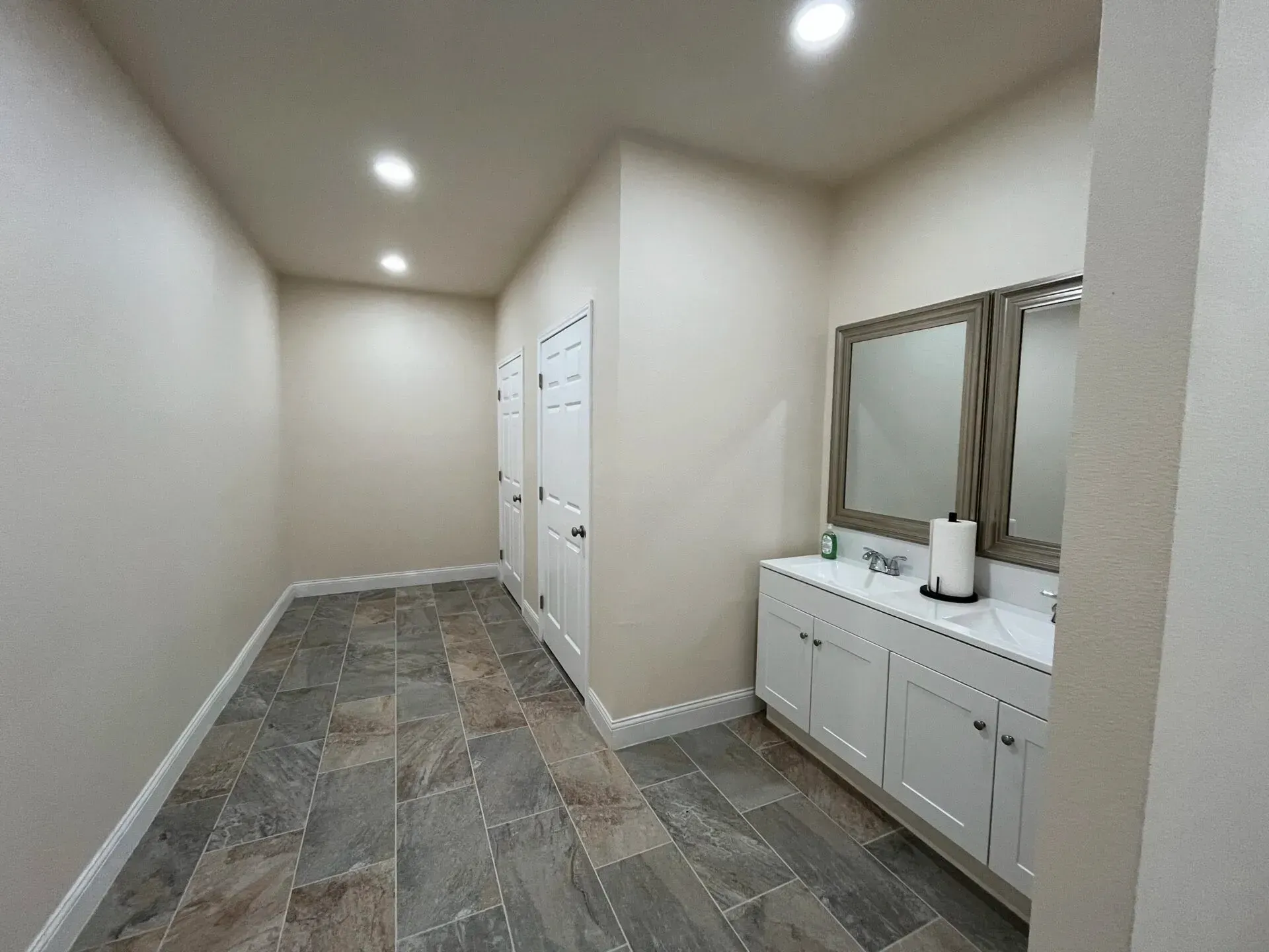 Modern hallway with white cabinets, mirrored vanity, recessed lights, and patterned tile floor.