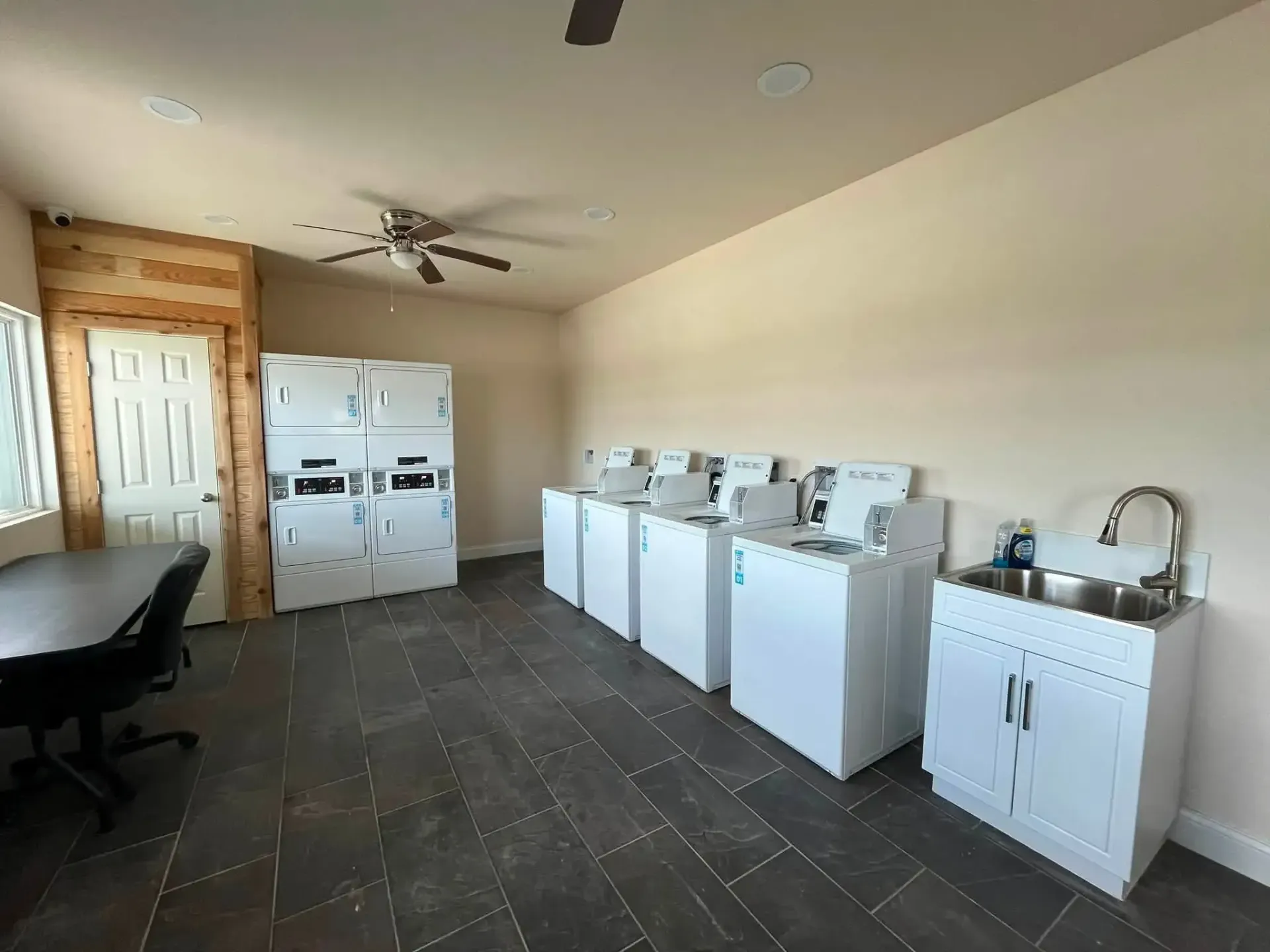 Laundry room with four white washers, utility sink, and table near a window and door
