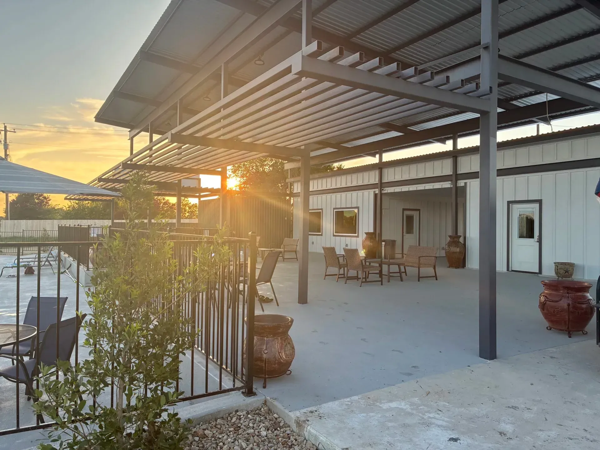 Sunset over an empty pool deck with patio table, chairs, and a closed umbrella ליד the pool