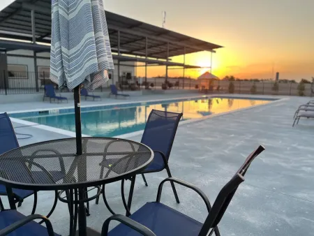 Outdoor pool at sunset with patio tables and chairs, a closed umbrella, and a covered pavilion.