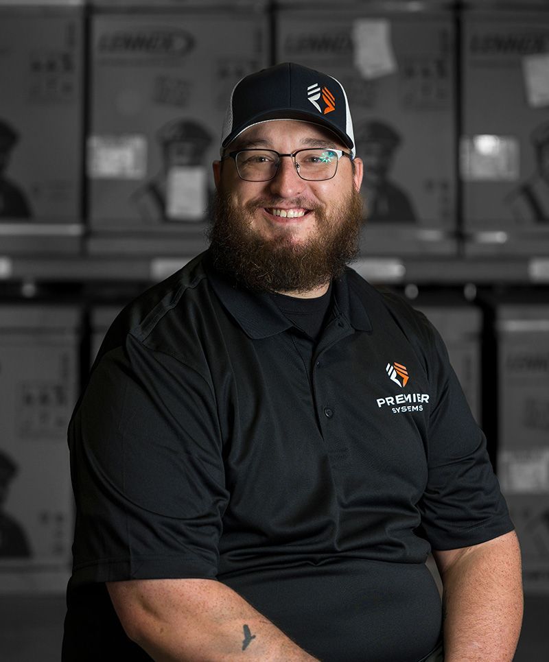 Man wearing a black hat and shirt with a company logo, smiling in front of boxes.