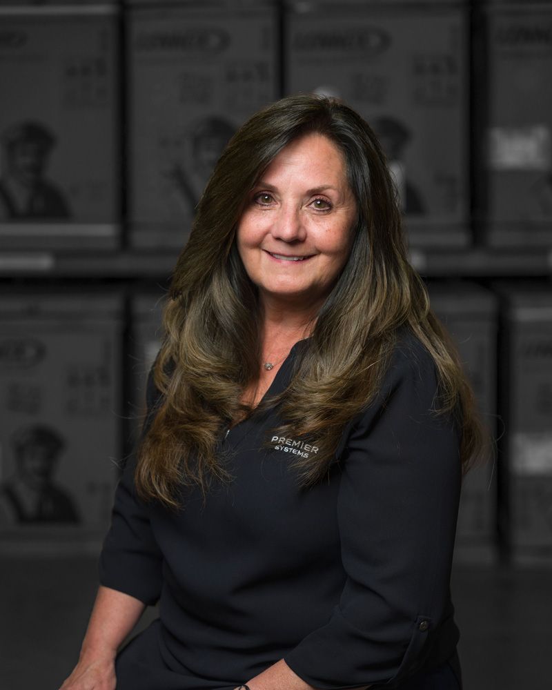 Woman with brown hair in black top, smiling, boxes in background.