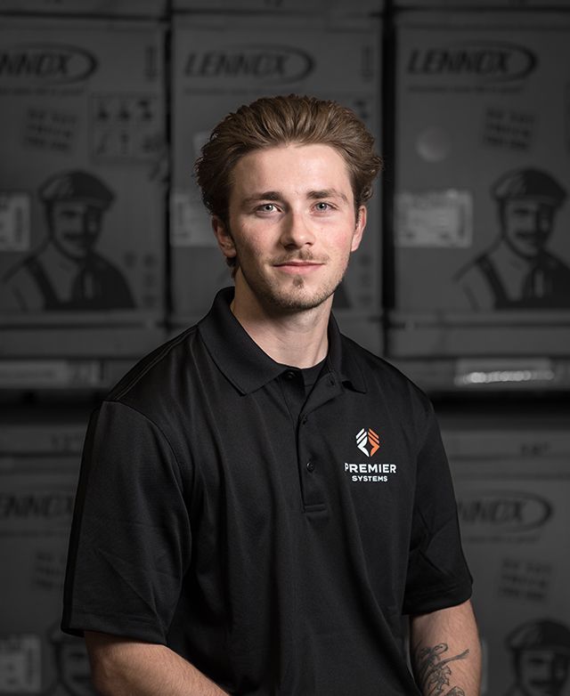 Man in black polo shirt stands in front of Lennox boxes, smiling. Logo on shirt reads