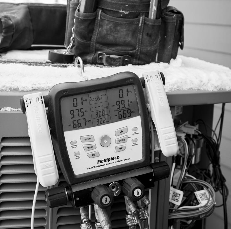 Black and white photo of a Fieldpiece HVAC digital manifold gauge, showing pressure readings on a snowy outdoor unit.