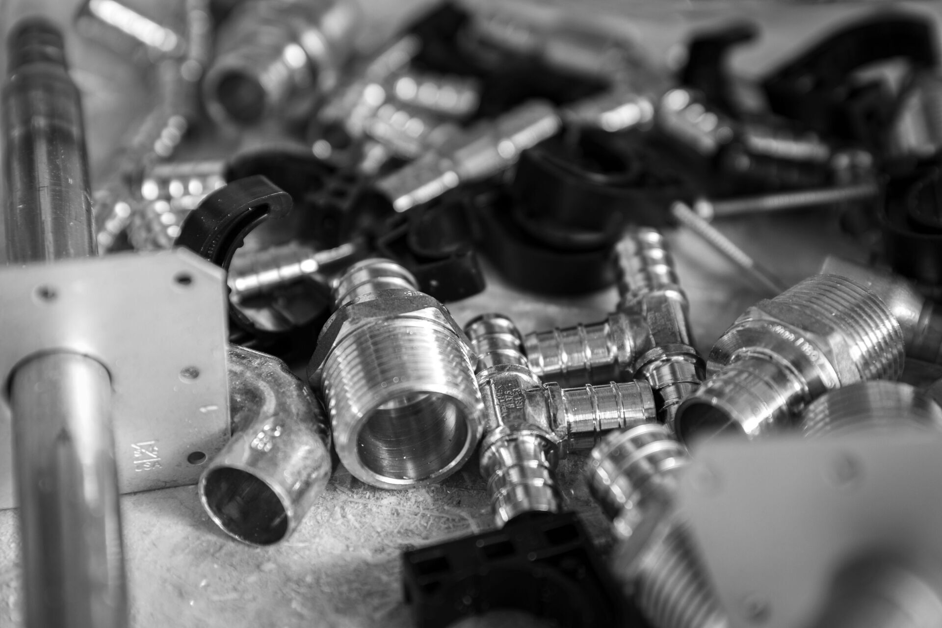 Close-up of assorted metal plumbing fittings and connectors, in grayscale.