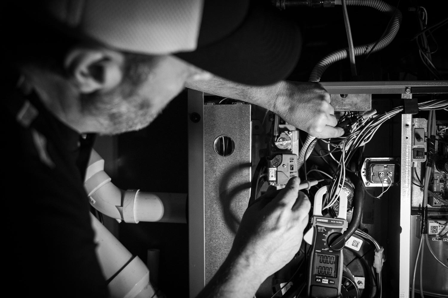Man in cap working on electrical panel, using a tool. Black and white.
