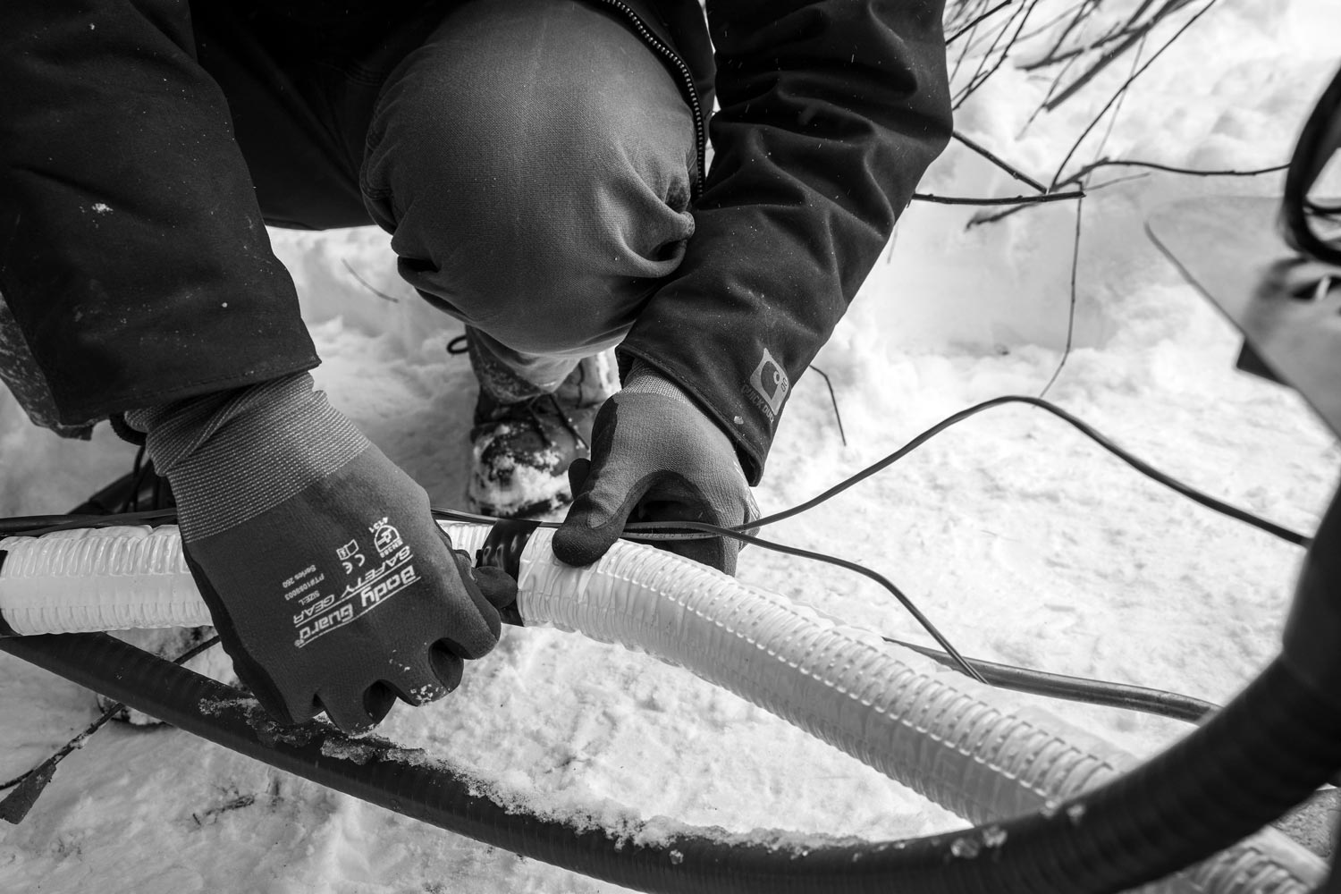 Person in gloves connecting white, corrugated tubing in snowy conditions.