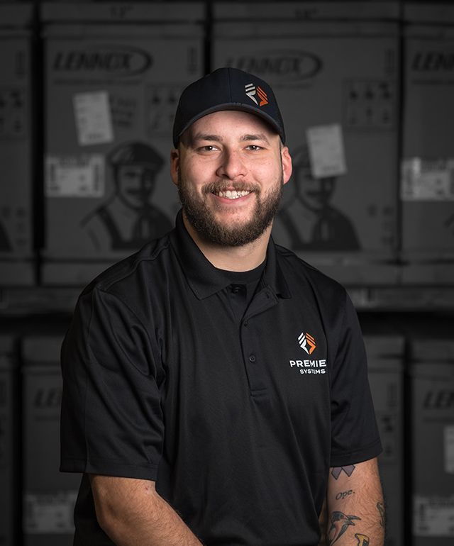 Man in black uniform smiles in front of boxes, wearing a cap with a logo.