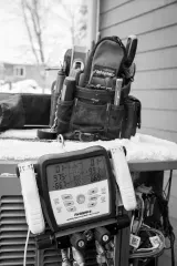 HVAC technician's tool bag and digital gauge on a unit outdoors, displaying pressure readings.