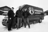 Three people pose with a Premier Systems van in snowy conditions. Black and white.