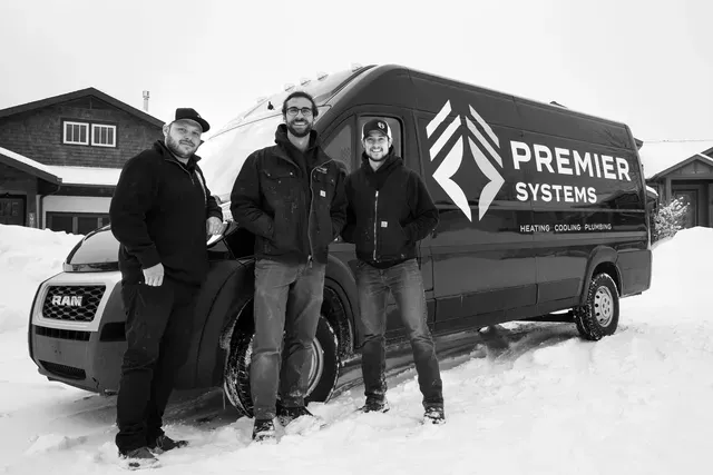Three people standing in front of a Premier Systems van in a snowy environment.